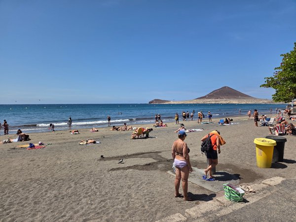 Bañistas tomando el sol y disfrutando del mar en Playa El Médano un día despejado.