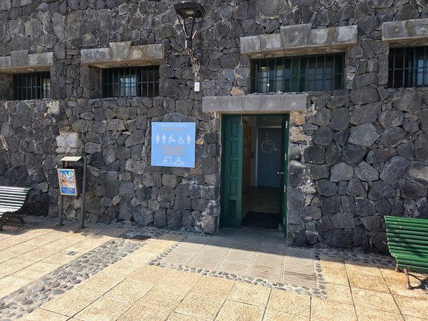 Entrada accesible a los baños públicos de Punta Brava integrados en un muro de piedra volcánica.
