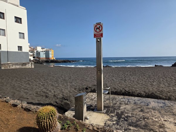 Ducha playera de acero inoxidable sobre la arena con señal de prohibido perros en la playa.
