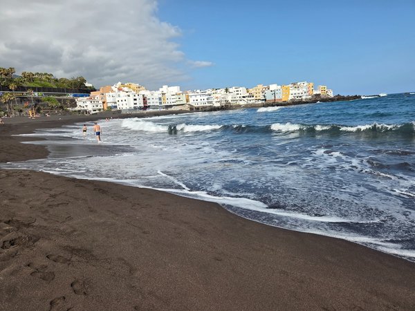 Olas rompiendo suavemente en la orilla de Punta Brava con las coloridas casas costeras del barrio al fondo.