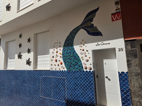Fachada decorada con mural de cola de sirena y conchas marinas en una calle cercana a la playa.